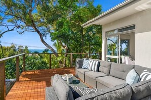 Un balcon avec un canapé gris, des coussins et une petite table sur laquelle sont posés deux bols blancs.
