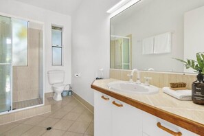 A modern bathroom with a glass shower enclosure, a white toilet, a sink with a wooden countertop, and a large mirror.