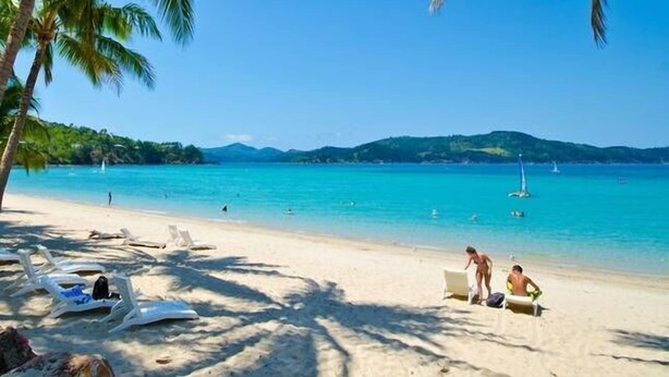 A beach with white lounge chairs and a few people. - Hibiscus 107 - Hamilton Island (Whitsundays)