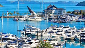 A marina with numerous boats docked, a prominent building with a modern design, and a clear view of the surrounding water and distant mountains. - Hibiscus 107 - Hamilton Island (Whitsundays)