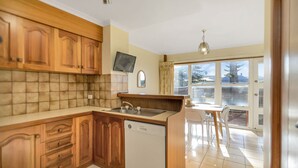 A kitchen with wooden cabinets, a dishwasher, and a dining area with a table and chairs. - Beautiful Beach Front Townhouse (Victor Harbor)