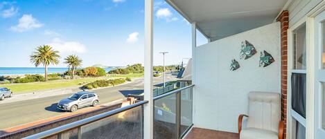 A balcony with a view of a road, palm trees, and a building with decorative fish wall art.