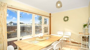 A dining area with a wooden table, white chairs, and large windows offering a view of the outside. - Beautiful Beach Front Townhouse (Victor Harbor)