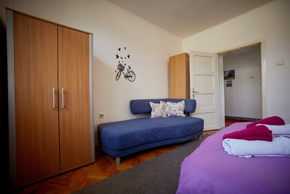 Un dormitorio con un sofá azul, una cama con ropa de cama púrpura y un armario de madera.