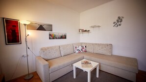 Een woonkamer met een beige modulaire bank, een witte salontafel, een vloerlamp en wanddecoratie.
