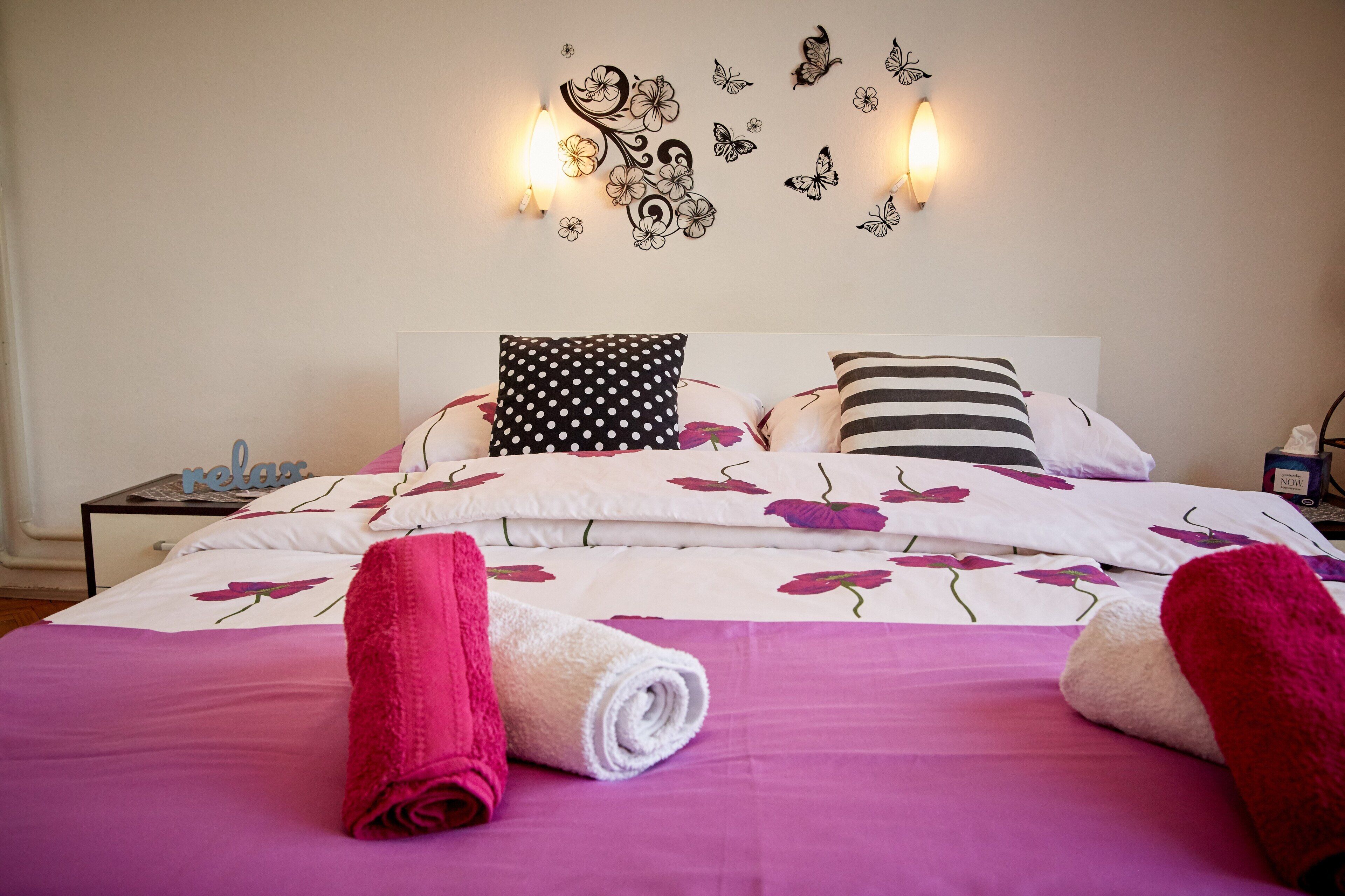 A neatly made bed with floral bedding, two pillows, and rolled towels.