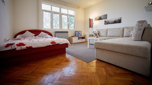 Een slaapkamer met een bed, een bank, een radiator, een televisie en een raam.