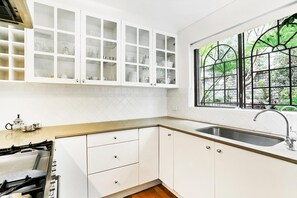 Enjoy a kitchen with a large window offering a view of lush greenery, stainless steel sink, and gas stove with a range hood.