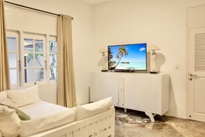 A room with a bed, a television on a cabinet, and a view of the beach through the window.
