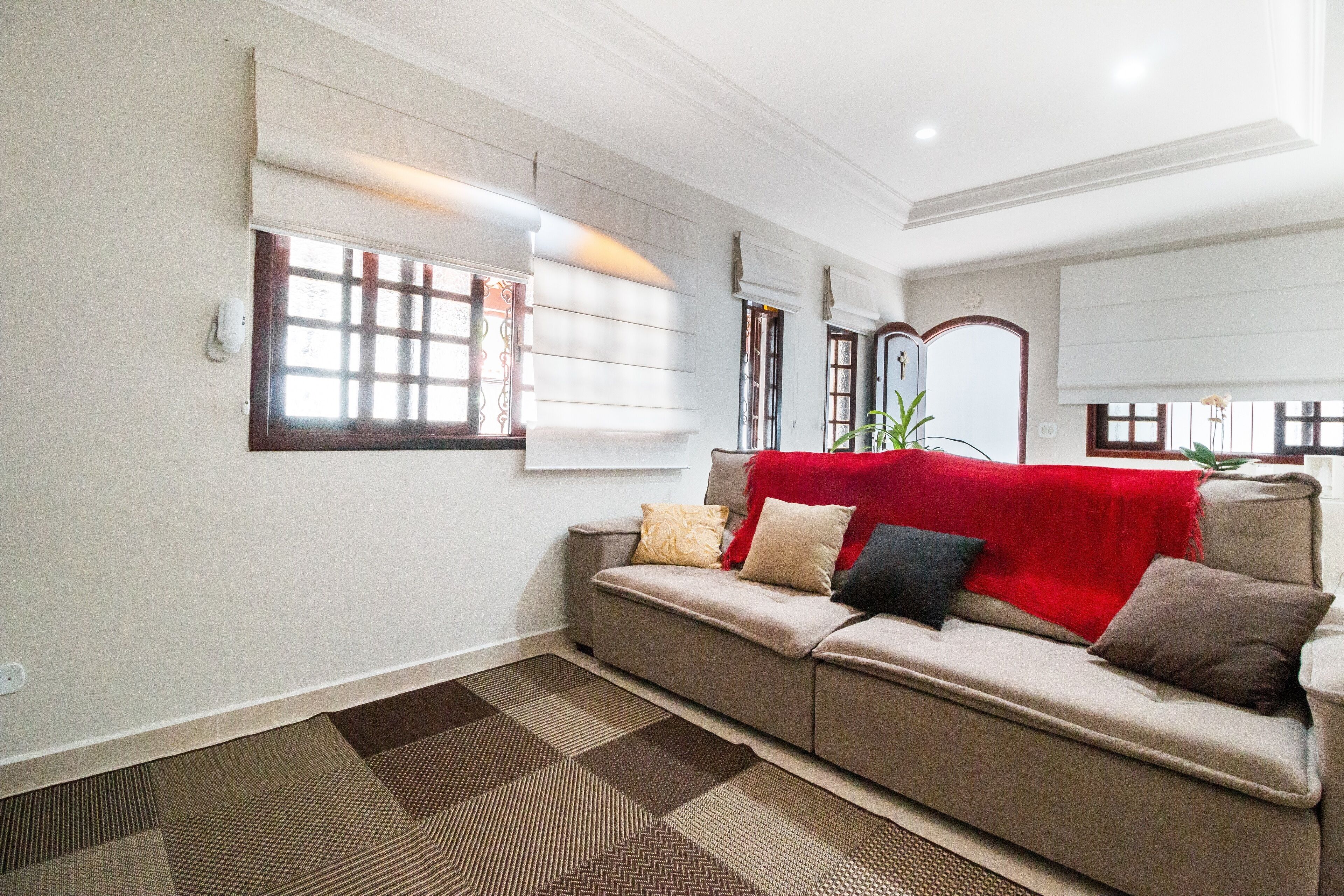 A living room with a beige sofa, patterned rug, and a red throw blanket.