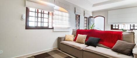 A living room with a beige sofa, patterned rug, and a red throw blanket.