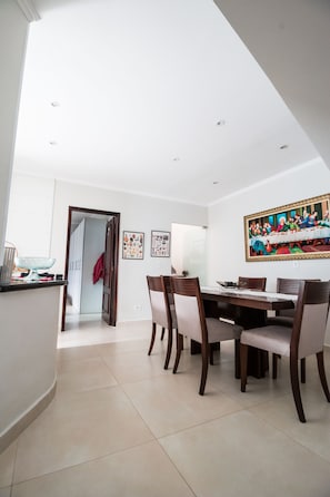 Un espace repas avec une longue table et des chaises, un tableau accroché au mur, et un coin cuisine avec un évier et un plan de travail visibles.