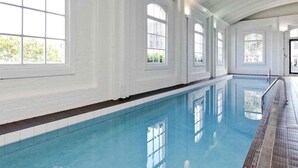 Una piscina interior con paredes blancas y ventanas amplias.