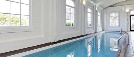 An indoor swimming pool with white walls and large windows.