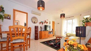 A living room with a wooden dining table, chairs, a TV, and a decorative rug. - Cosy flat on second floor with large pool (Orihuela)