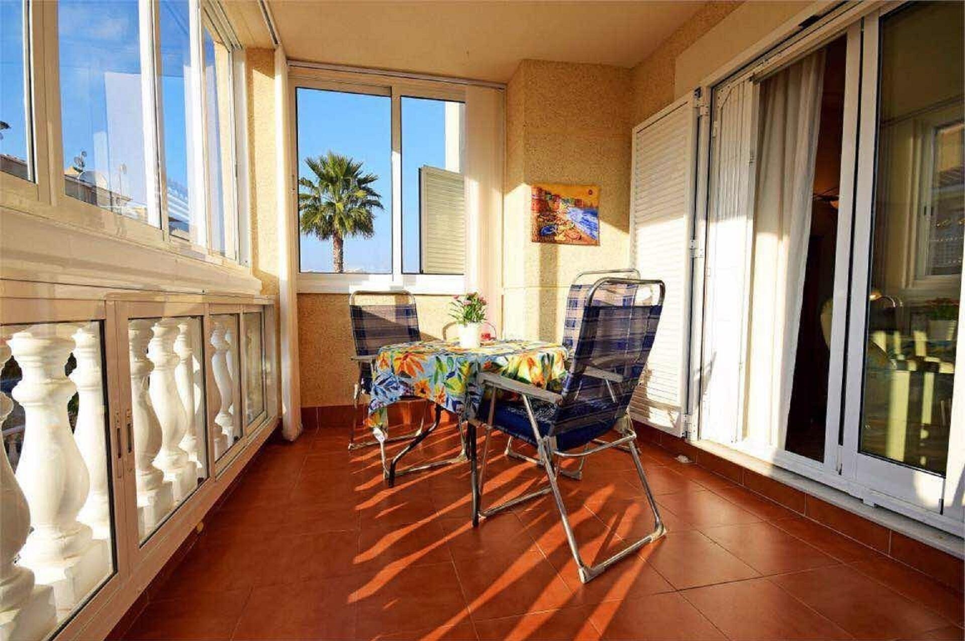 Un balcone con tavolo e sedie, una pianta in vaso e un quadro appeso al muro.