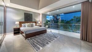Quarto moderno com cama grande, mesas de cabeceira, um criado-mudo, tapete estampado e uma varanda com vista para árvores e céu noturno.