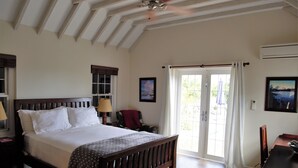 A bedroom with a wooden bed, a ceiling fan, a desk, and a view through a glass door. - Wild Bird, Paget - Pool, Twizy charger, Kitchenette -  non smoking property (Paget)