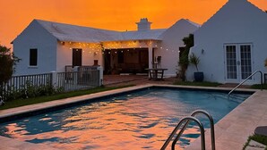 A white house with a swimming pool and a patio area. - Wild Bird, Paget - Pool, Twizy charger, Kitchenette -  non smoking property (Paget)