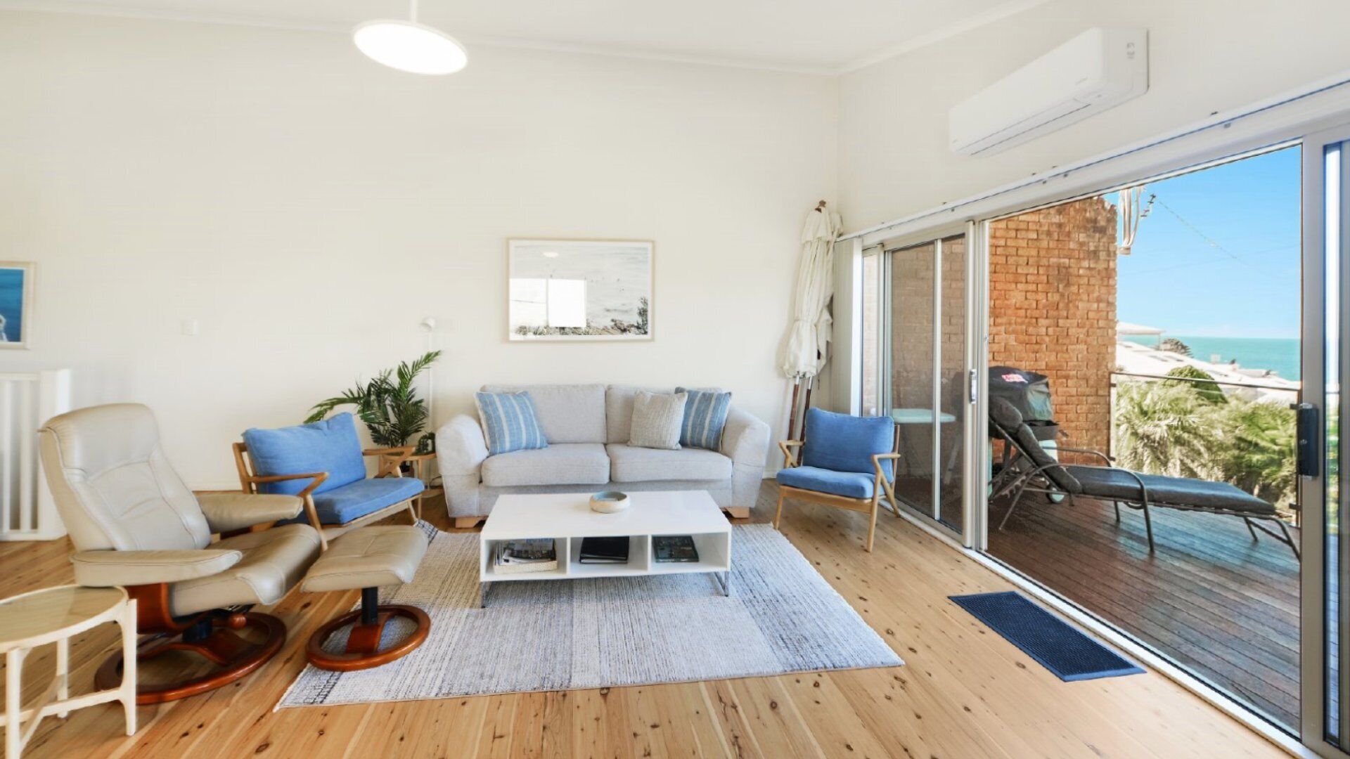 A spacious living room with a large window offering a view of the sea, a comfortable seating area with a sofa and chairs, and a small coffee table.