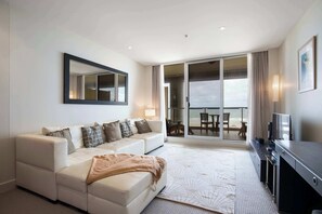 Et moderne hotelværelse med sofa, fladskærms-TV, stort vindue og skydedør med glas ud til en balkon.