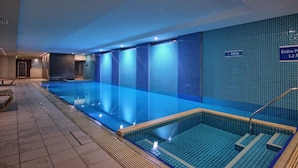 An indoor swimming pool with a tiled wall, a sign indicating the pool's location, and a separate shallow area. - Ocean View 1BR Private balcony OAKS PIER (Glenelg)