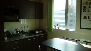 A small kitchen with a microwave, sink, and cabinets. There is a window with a view of buildings outside. - Private Apartment in Quito's Best Neighborhood (Quito)