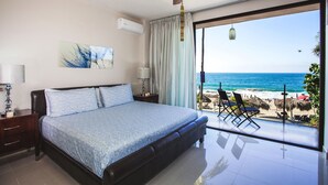 A bedroom with a bed, a ceiling fan, a nightstand, a lamp, and a large window with a view of the beach and ocean. - Beachfront right on Los Muertos beach (Amapas)