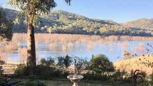 A serene lakeside view with a statue in the foreground, surrounded by lush greenery and hills in the background.