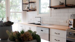 A modern kitchen with white cabinets, a wooden countertop, a built-in oven, and a window overlooking greenery.