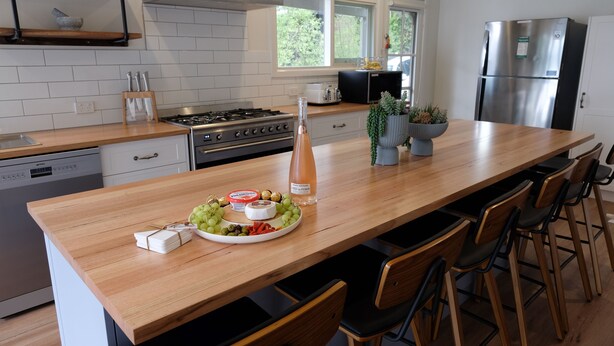 A modern kitchen with a wooden countertop, a stainless steel refrigerator, and a dining area with chairs.