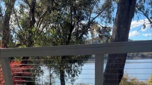 A table with a bottle of Heineken beer, a bowl of chips, and a glass of wine on a deck with a view of a lake and trees.