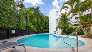 Una piscina con una escalera metálica, rodeada de palmeras y una valla de madera.