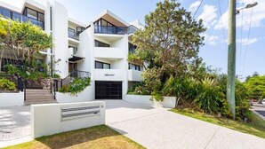 Un edificio moderno con fachada blanca, varios balcones y un jardín bien cuidado.