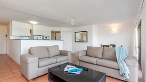 Una sala de estar moderna con dos sofás, una mesa de centro y una cocina al fondo.