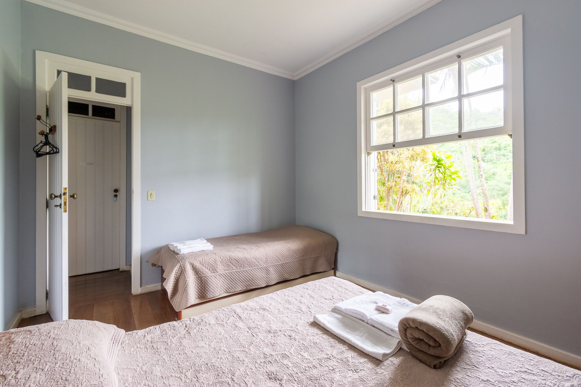 Una camera da letto con due letti, una finestra vista verde e una porta che dà su un'altra stanza.
