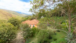 Una casa con techo de tejas rojas rodeada de abundante vegetación y colinas al fondo.