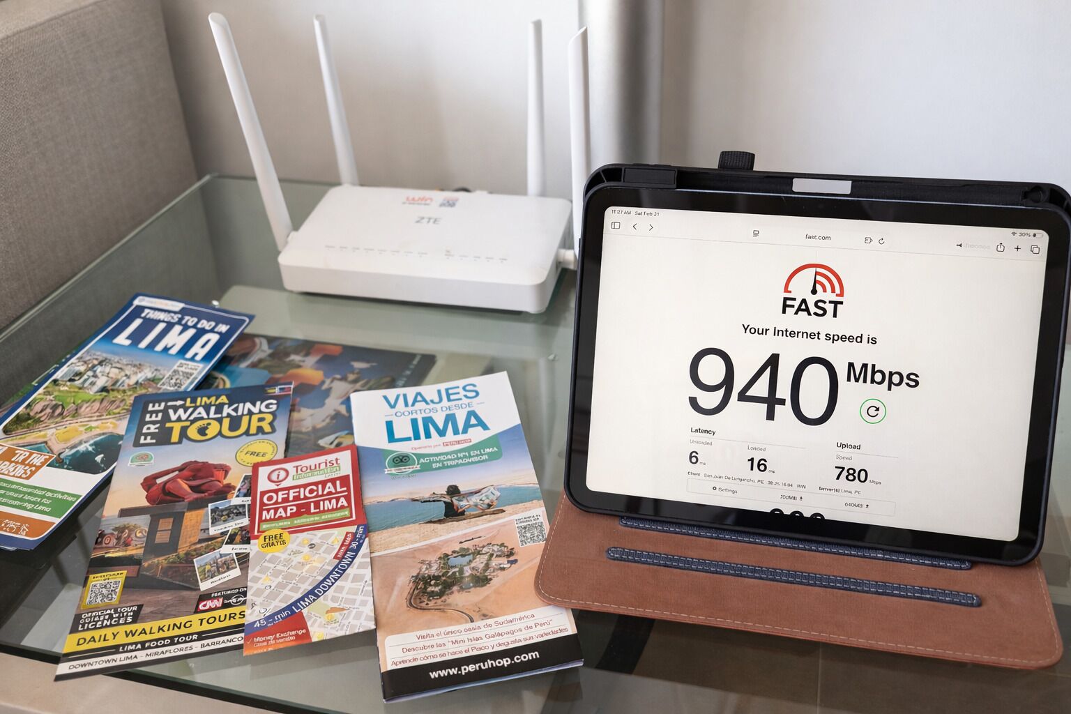Une tablette affichant la vitesse de la connexion Internet, un routeur et des brochures de voyage, le tout posé sur une table.