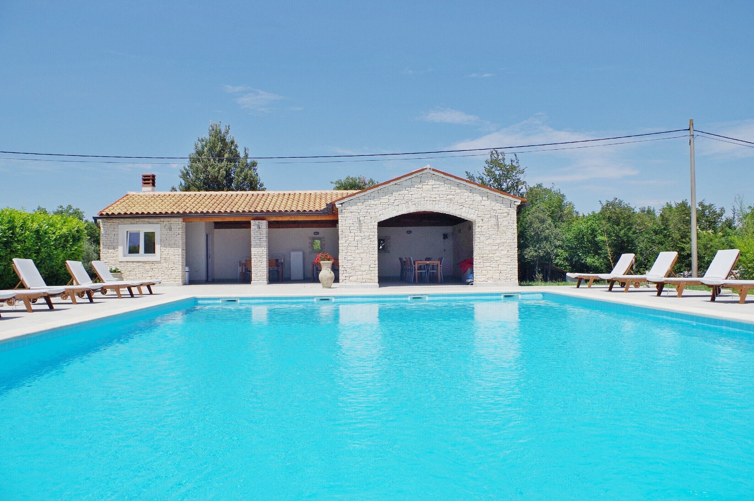 Un edificio junto a la piscina, con fachada de piedra, garaje cubierto y piscina azul cristalina.