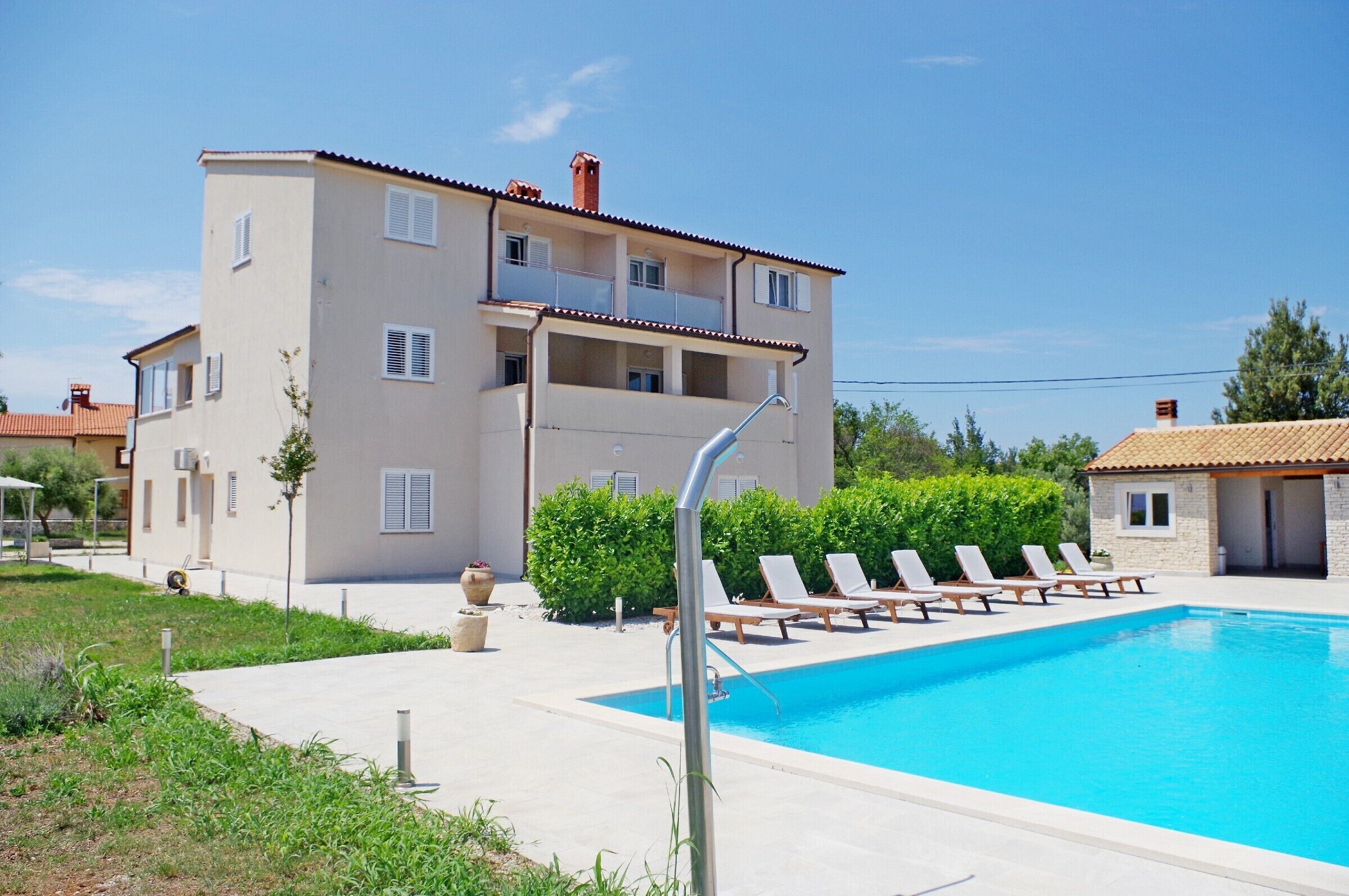A two-story building with a swimming pool, lounge chairs, and a clear sky.