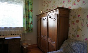 Une chambre avec une armoire en bois, un lit avec une literie à motifs, un radiateur et une fenêtre avec des rideaux.