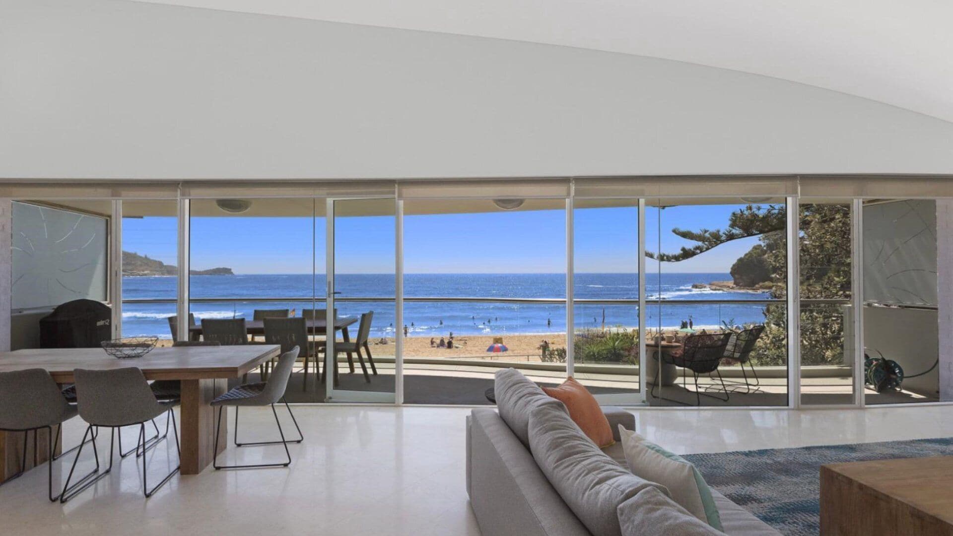 Ein modernes Wohnzimmer mit einer großen Glaswand und Blick auf den Strand und den Ozean.