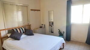 Un dormitorio con cama, mesita de noche, espejo, armario y ventana con cortinas.