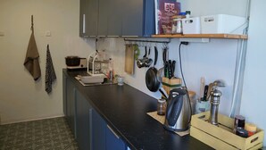Una cocina con encimera negra, utensilios colgantes, hervidor y cafetera.
