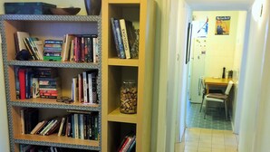 Un pasillo estrecho con una estantería llena de libros, un farol y un tarro de tapones de corcho.