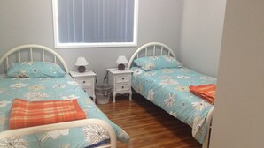 Un dormitorio con dos camas individuales, cada una con ropa de cama floral, una mesita de noche pequeña con una lámpara y una ventana con persianas.