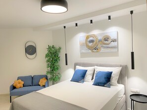 A modern bedroom with a bed, a sofa, a wall clock, a plant, and a painting.