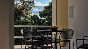 A balcony with a table and chairs, a bowl of fruit, and a view of trees and sky. - Xcaret. cómodo apartamento muy bien equipado. (Merida)
