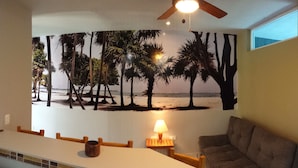 A room with a beach mural, a ceiling fan, a lamp, and a couch. - Xcaret. cómodo apartamento muy bien equipado. (Merida)