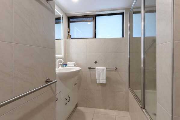 Un baño moderno con cabina de ducha de vidrio, lavamanos con toallero y ventana sobre el espejo.